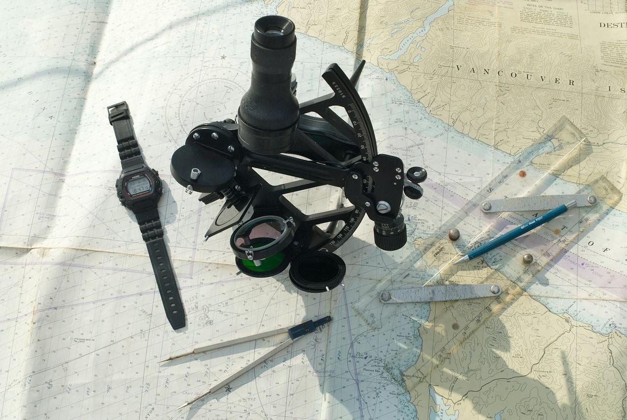 Sextant, dividers, parallel rule and watch laid on a paper nautical chart for passage planning